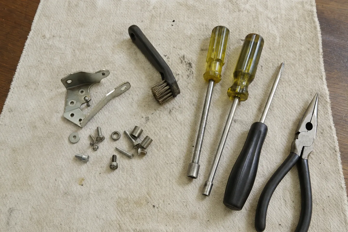 Hinge bracket, latch strike, nut drivers, pliers and fasteners laid out on a canvas cloth